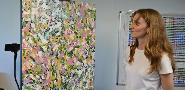 Artistas usam robôs de IA para reproduzir telas e aumentar Artista Audrey-Éve Goulet em seu estúdio no Canadá em frente à sua obra reproduzida por robô. "É impressionante. Fiquei surpresa de forma positiva"